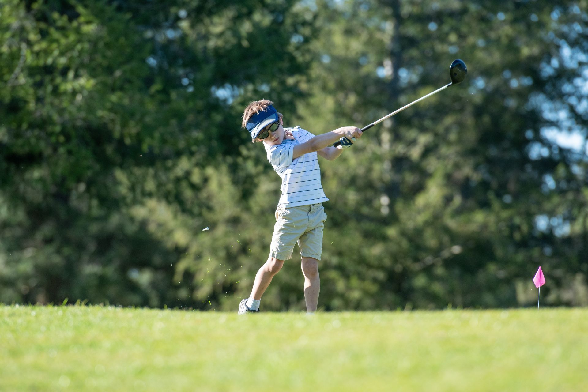 Golfer swinging a club on a sunny course, with a pink flag in the distance