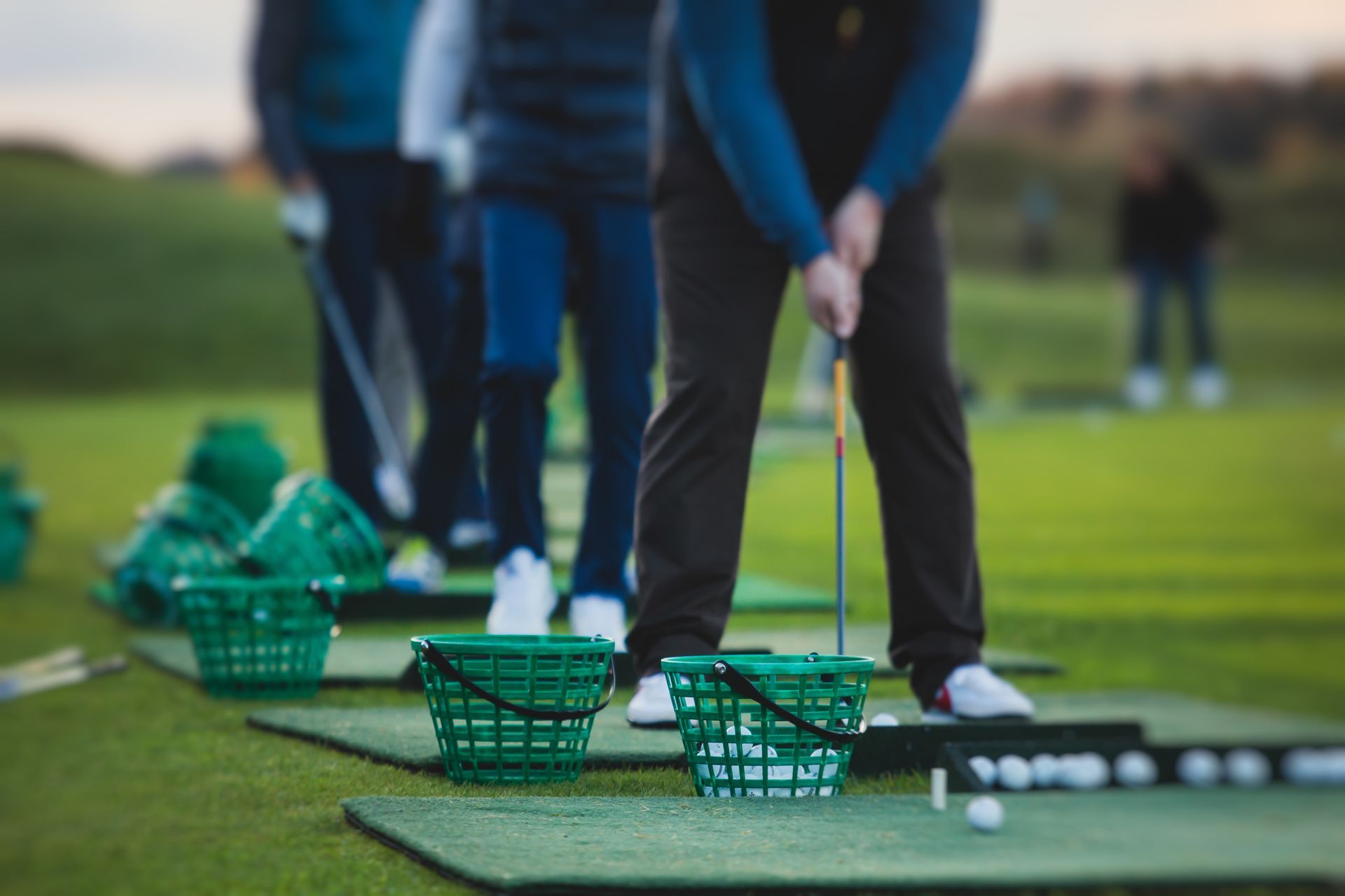 Golfers practicing driving on a green driving range with baskets of balls and clubs on the ground Golfers practicing driving on a green driving range with baskets of balls and clubs on the ground