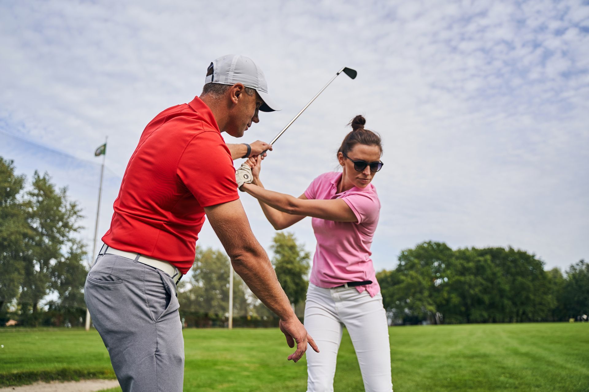 Two golfers practicing a swing on a grassy golf course, one in red and one in pink Two golfers practicing a swing on a grassy golf course, one in red and one in pink