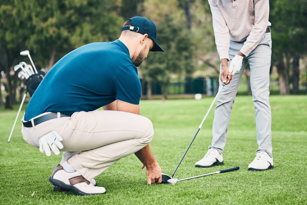Golfer crouching to line up a putt while another stands nearby on a green course Golfer crouching to line up a putt while another stands nearby on a green course
