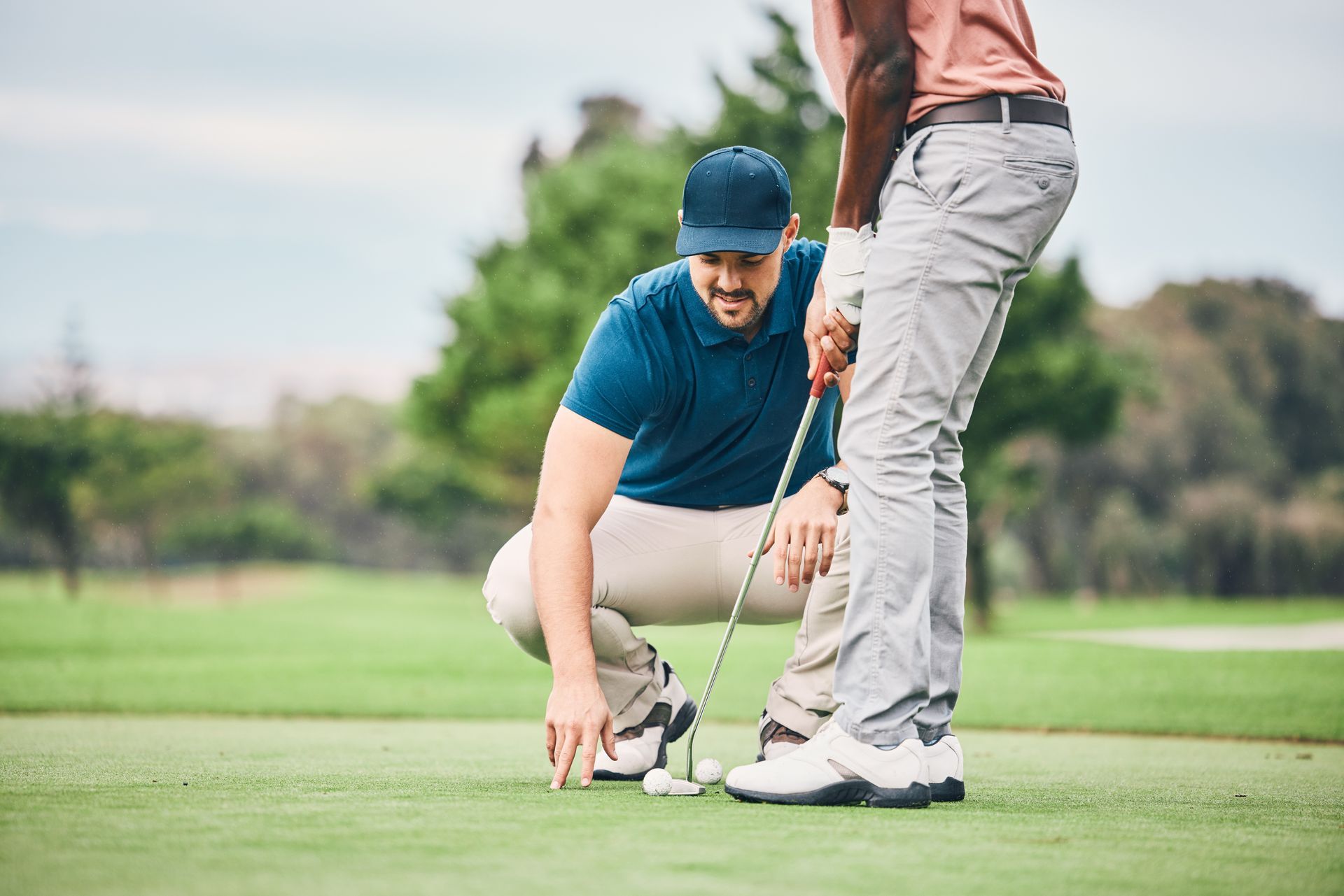 Two golfers lining up a putt on a green, one crouching to aim the ball Two golfers lining up a putt on a green, one crouching to aim the ball