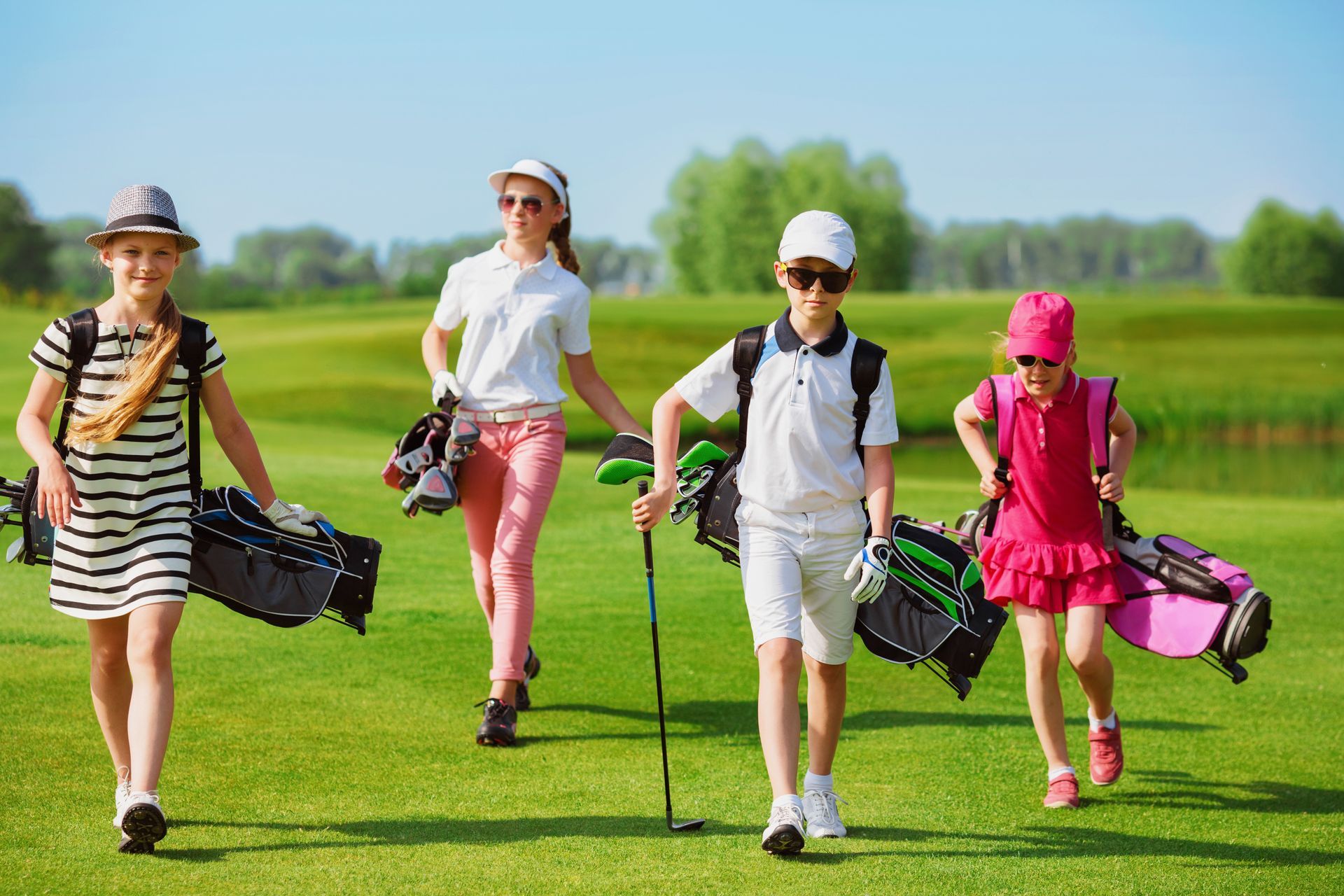 Four golfers walking across a green golf course with clubs and bags on a sunny day