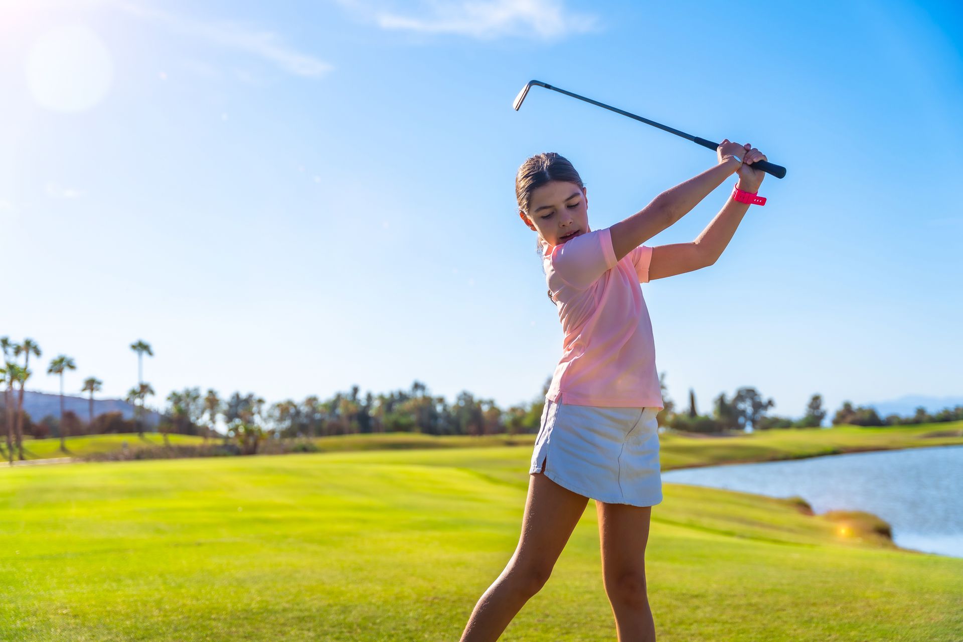 Golfer swinging a club on a sunny green course near water Golfer swinging a club on a sunny green course near water