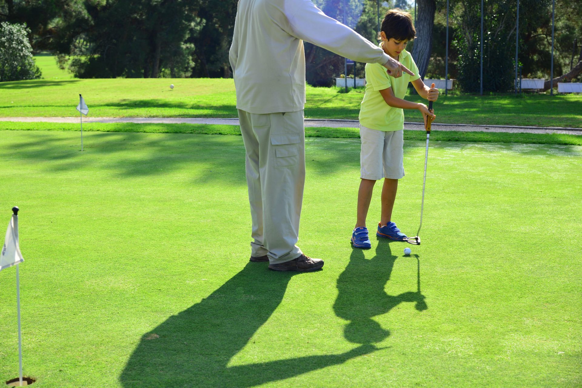 Adult helping child swing a golf club on a sunny green course