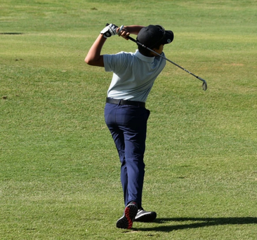 Golfer in white shirt and navy pants swinging a club on a grassy course