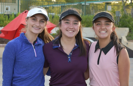 Three smiling people in golf attire standing outdoors on a course