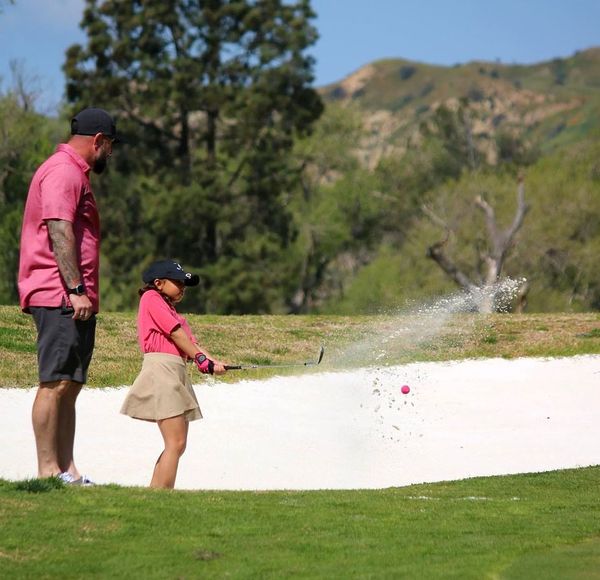 Two golfers in pink shirts spraying water from a hose on a golf course green Two golfers in pink shirts spraying water from a hose on a golf course green