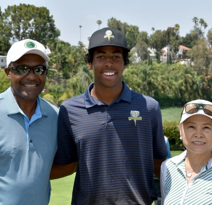 Three smiling people standing outdoors at a golf course, wearing caps and polo shirts.