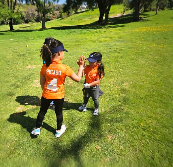 Two children in orange shirts high-five on a sunny grassy field. Two children in orange shirts high-five on a sunny grassy field.