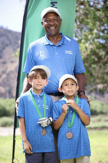 Three people in blue shirts and hats posing with medals at an outdoor event