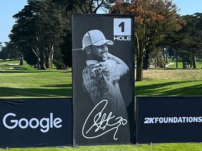 Golf tee sign with golfer silhouette, 1 HOLE, Google logo, and 2K Foundations logo on a course