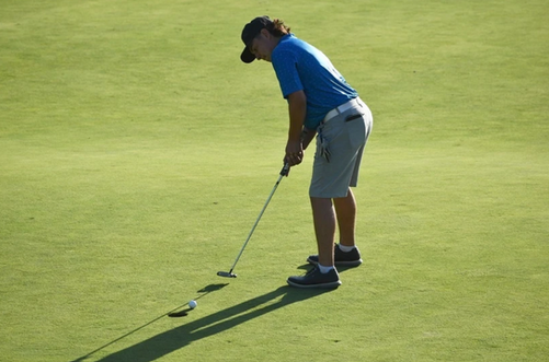 Golfer in blue shirt putting on a green golf course