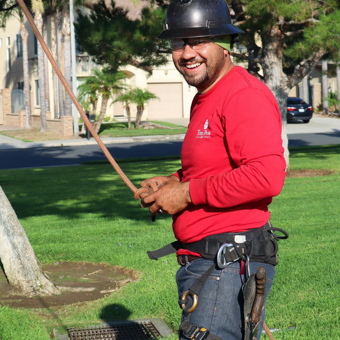 Utility worker in red shirt and hard hat smiling while holding a rope outdoors.