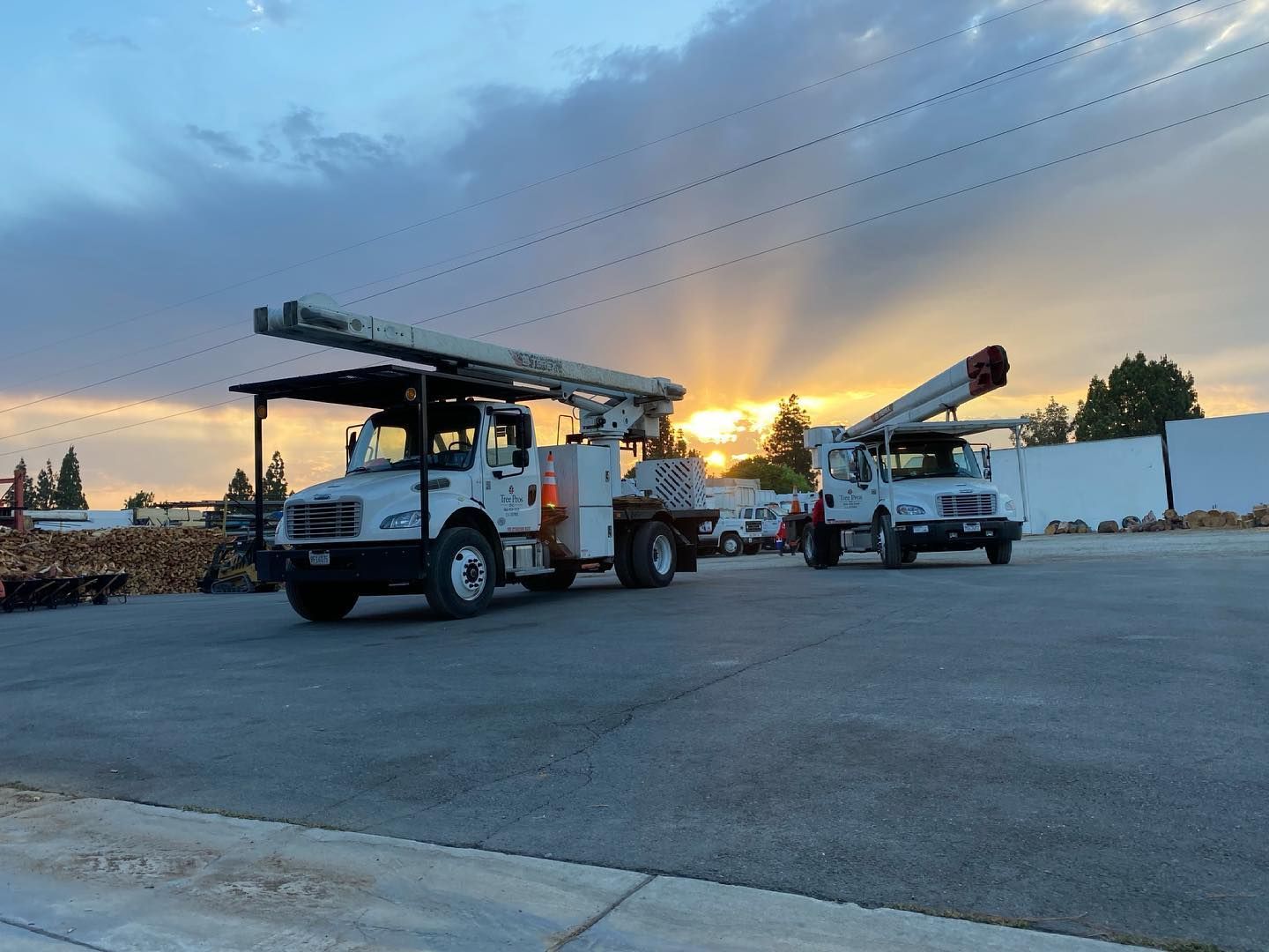 Two utility trucks with raised bucket lifts parked at sunset in an open lot