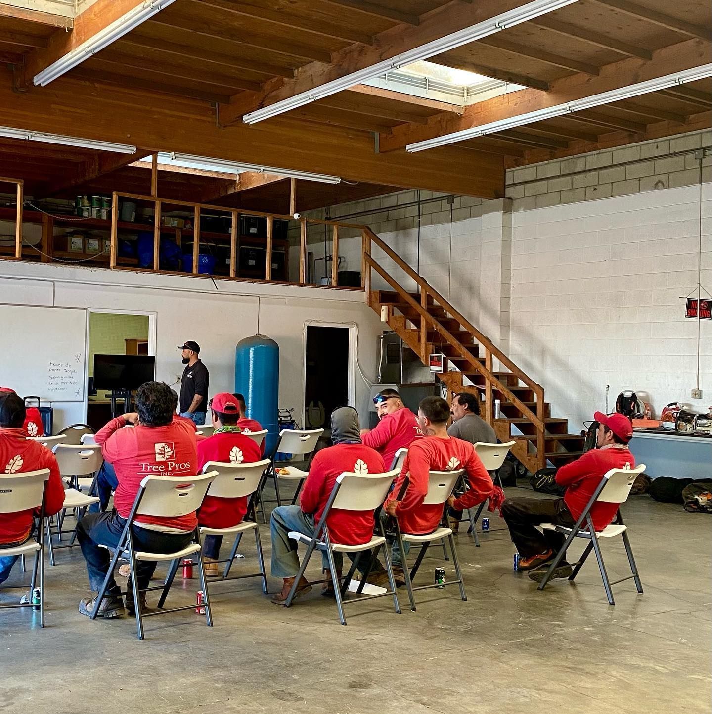 People in red shirts seated in folding chairs at a workshop inside a warehouse-like room