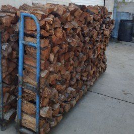 Stacked firewood on a blue hand truck beside a concrete walkway.
