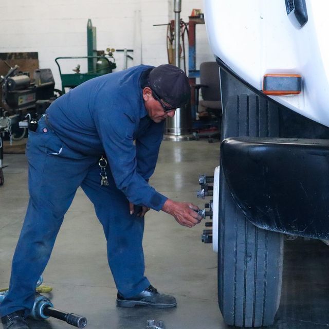 Mechanic in blue coveralls inspecting a large truck tire in a garage