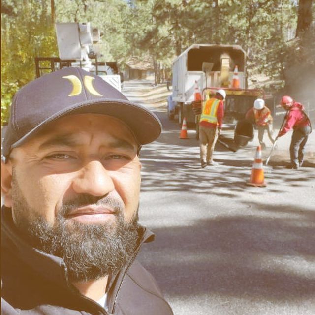 Man taking a selfie near roadwork crew paving a street beside an asphalt paver and cones