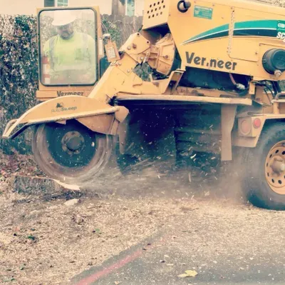 Yellow excavator tearing up concrete and dirt, kicking up dust outdoors