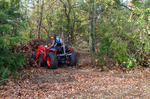 Red tractor with driver clearing leaves on a wooded trail in autumn