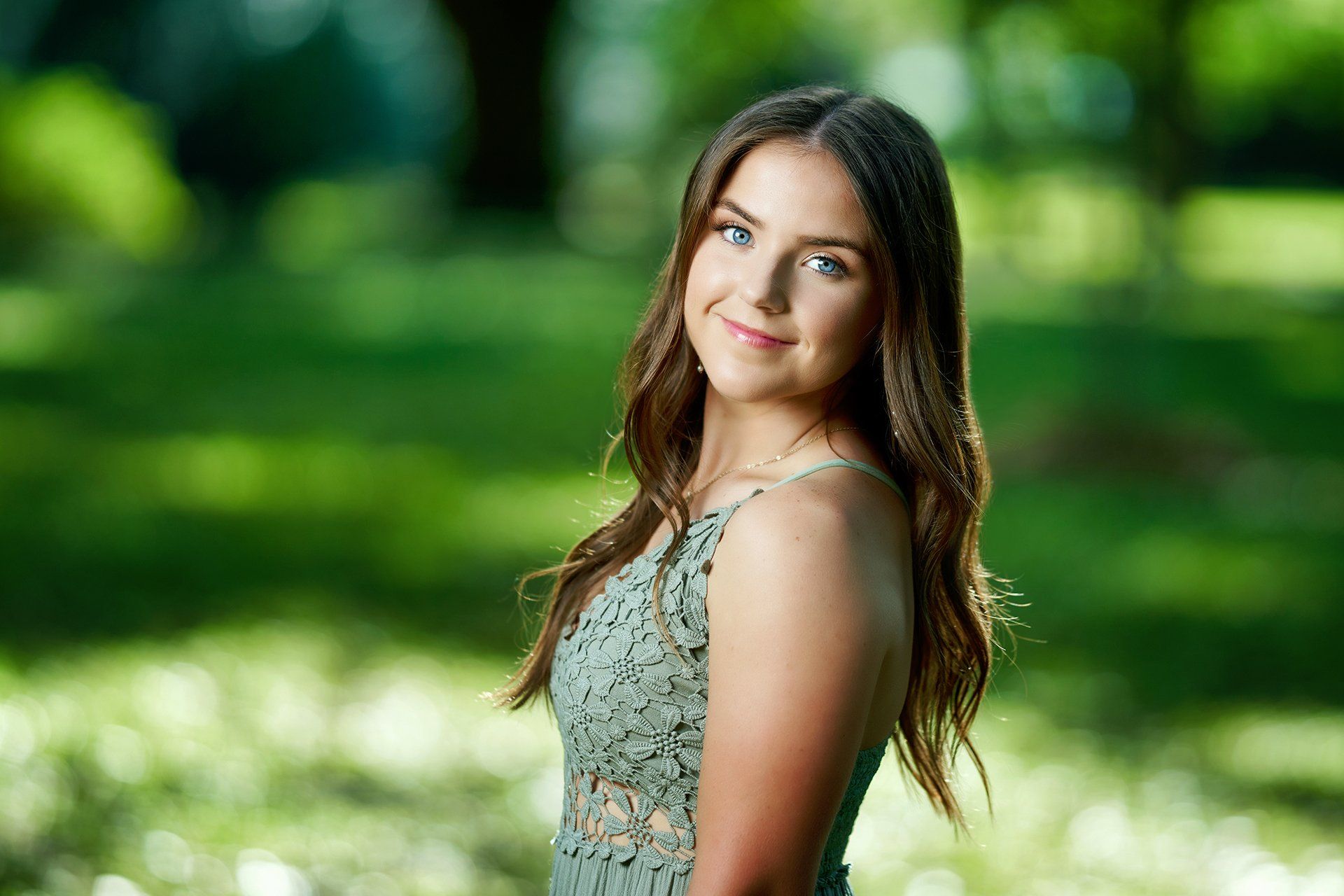 A young woman in a green dress is standing in a park.