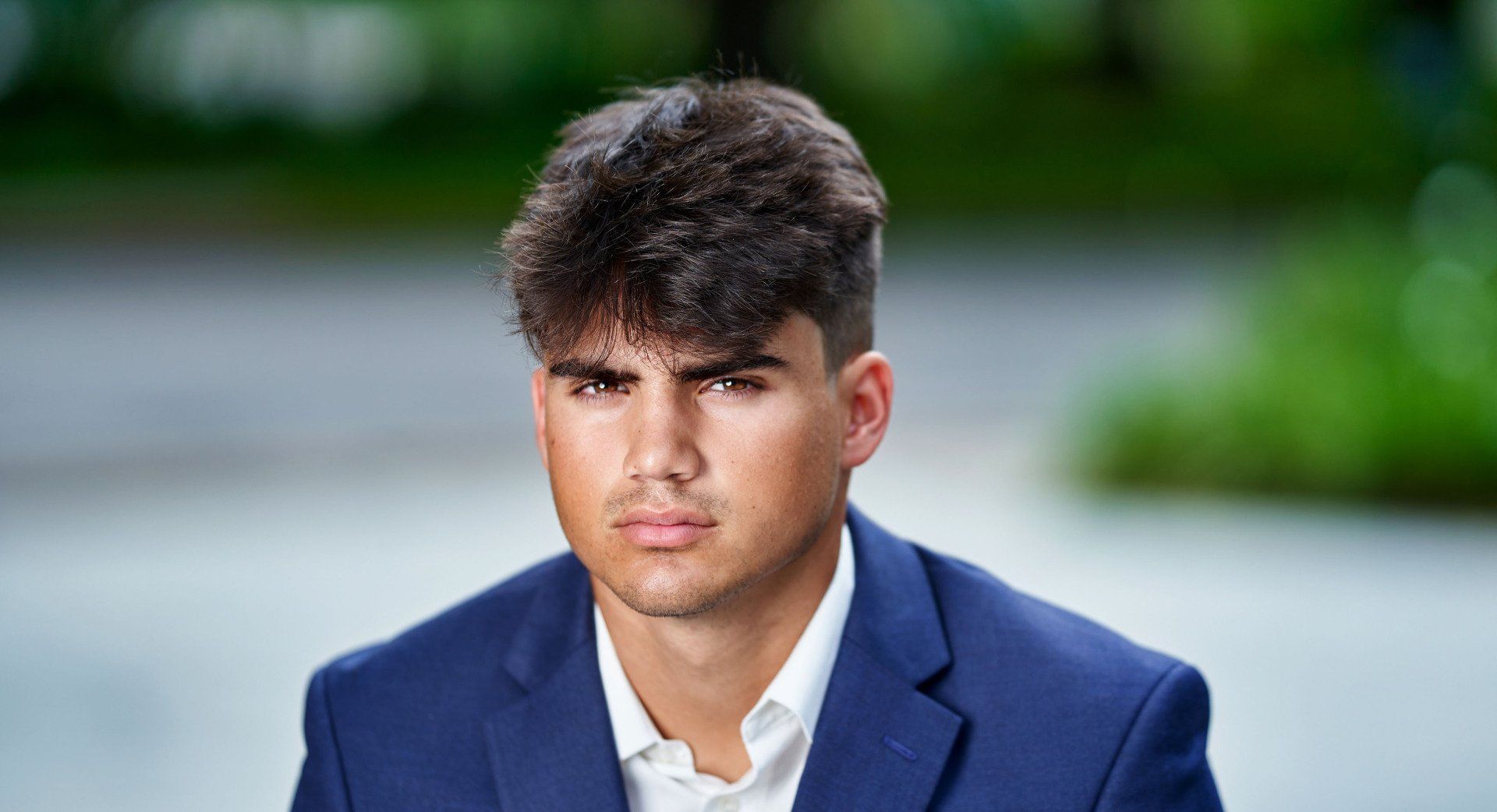 A young man in a blue suit and white shirt is looking at the camera.