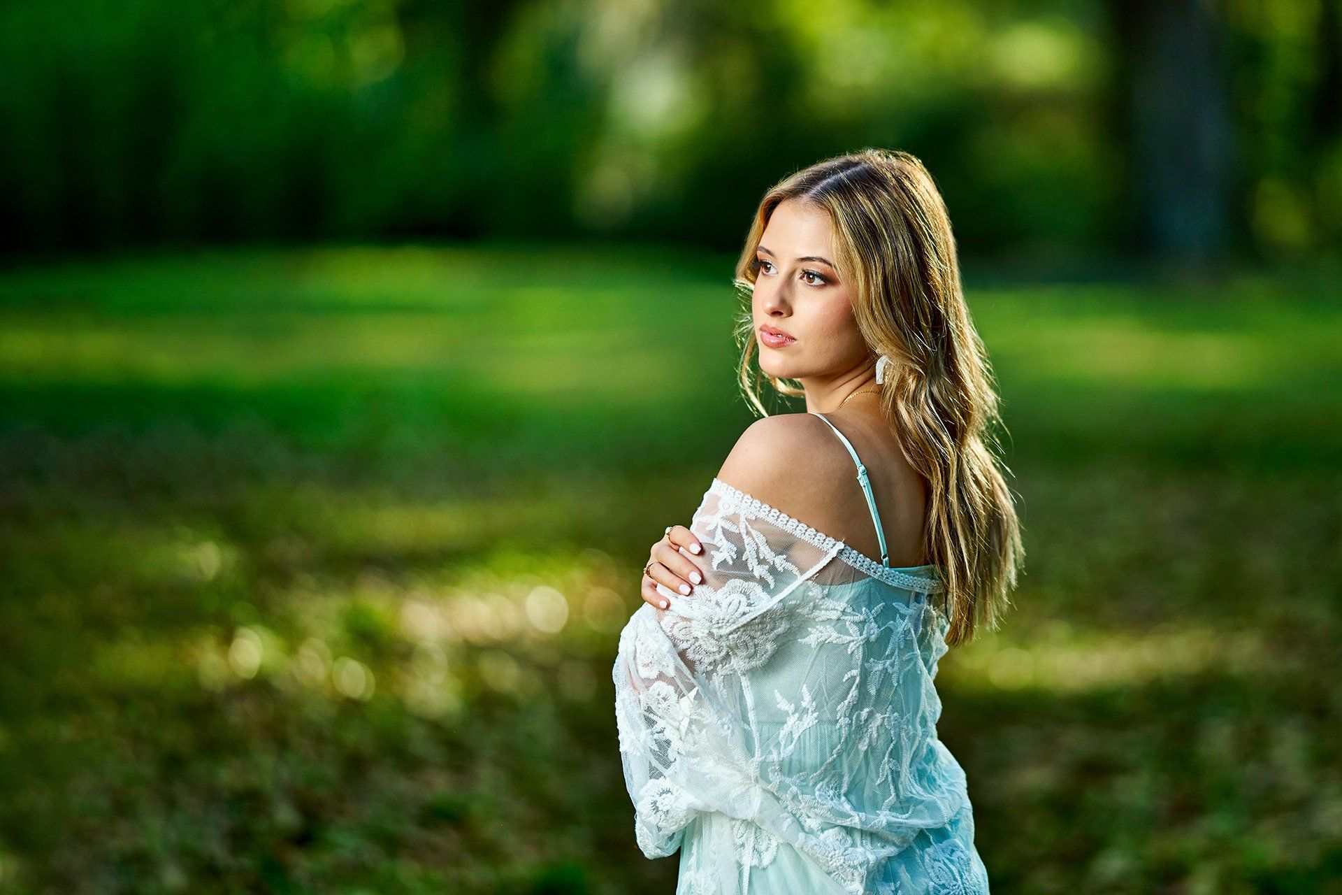 A woman in a white lace dress is standing in a park.