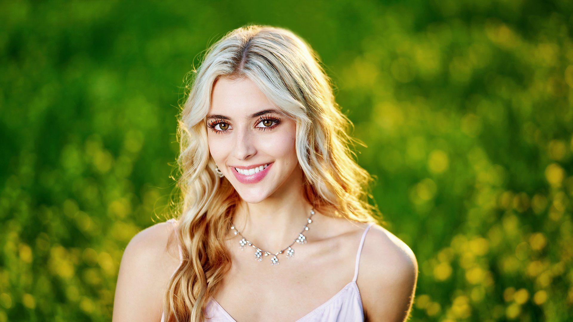 A woman in a pink dress and necklace is standing in a field of yellow flowers.