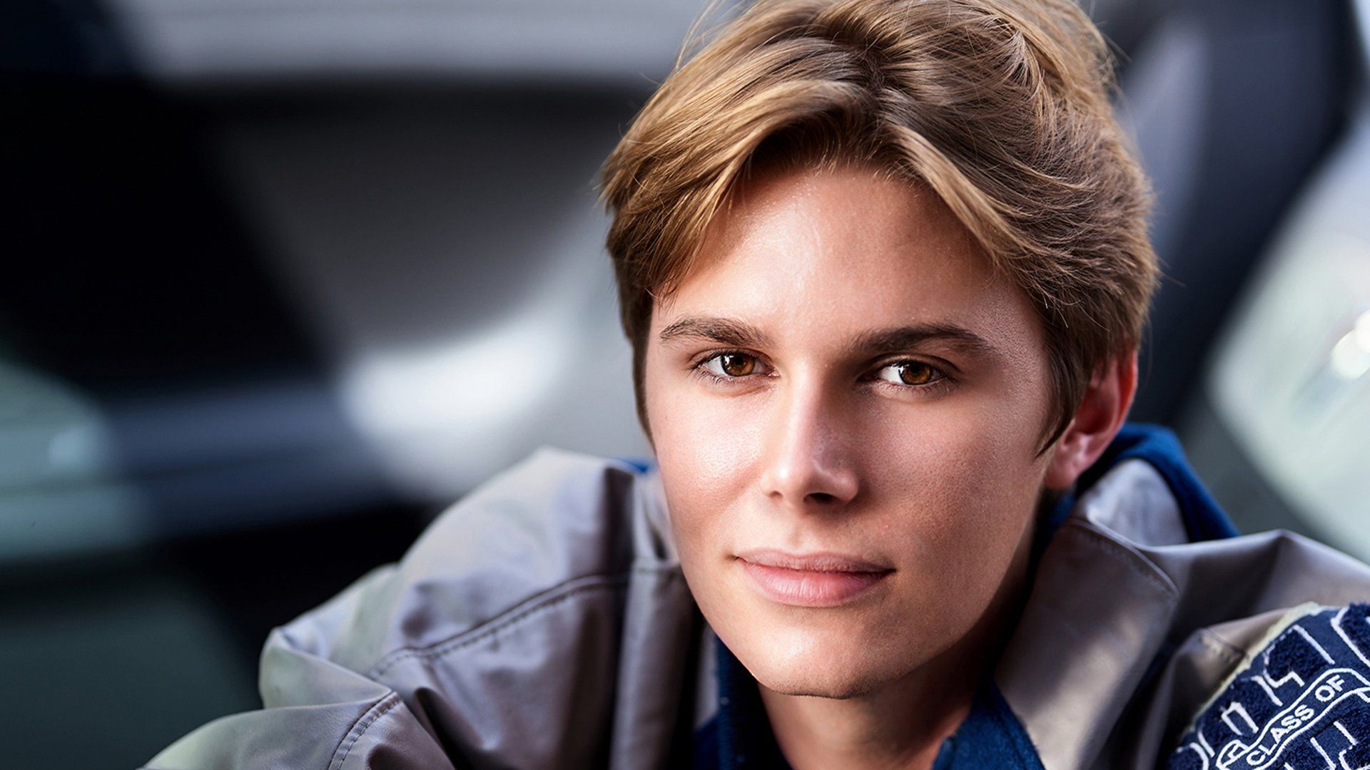 A young man is wearing a jacket and smiling for the camera.