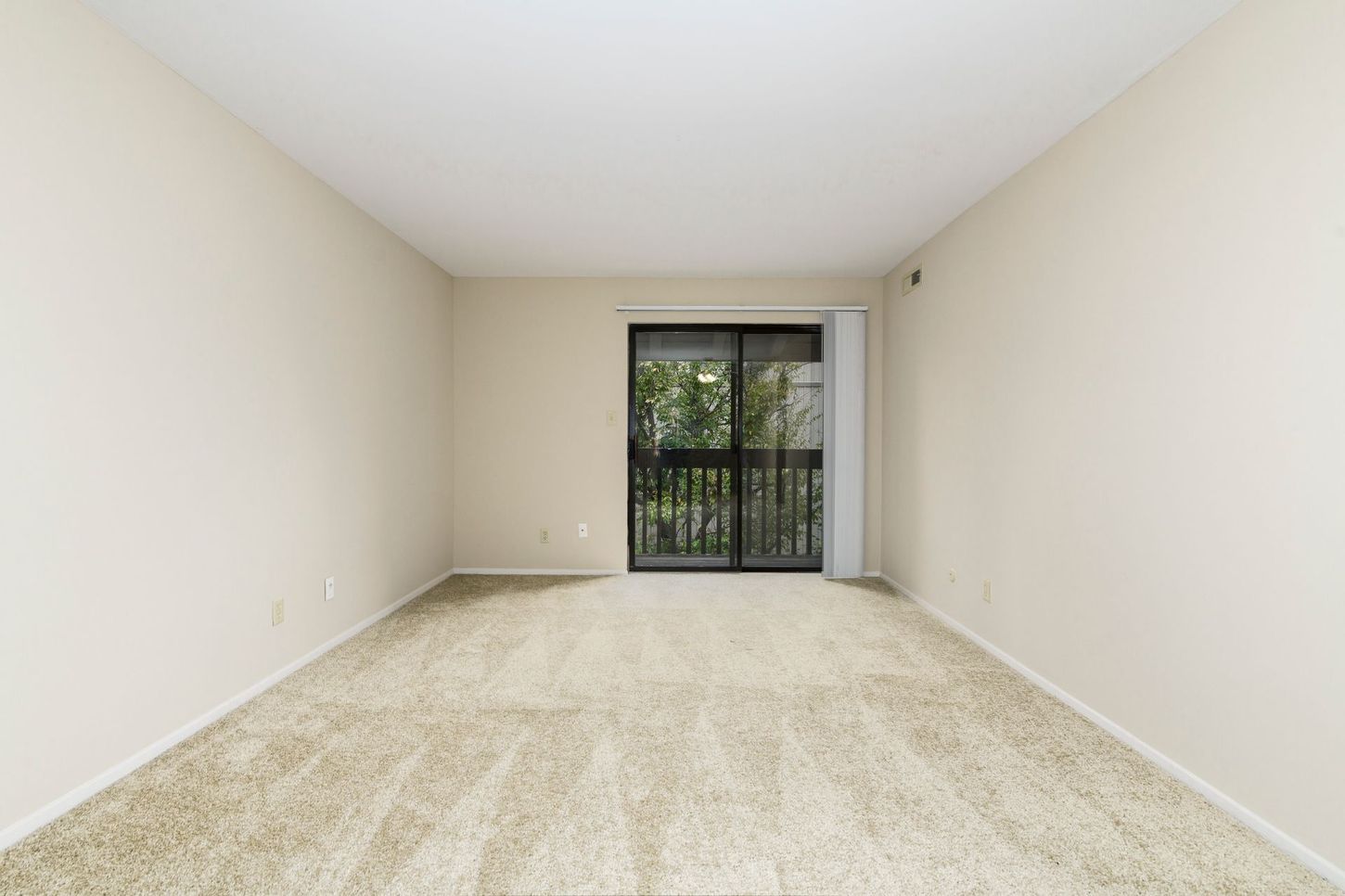 Empty room with tan carpet, beige walls, and a sliding glass door to a balcony.