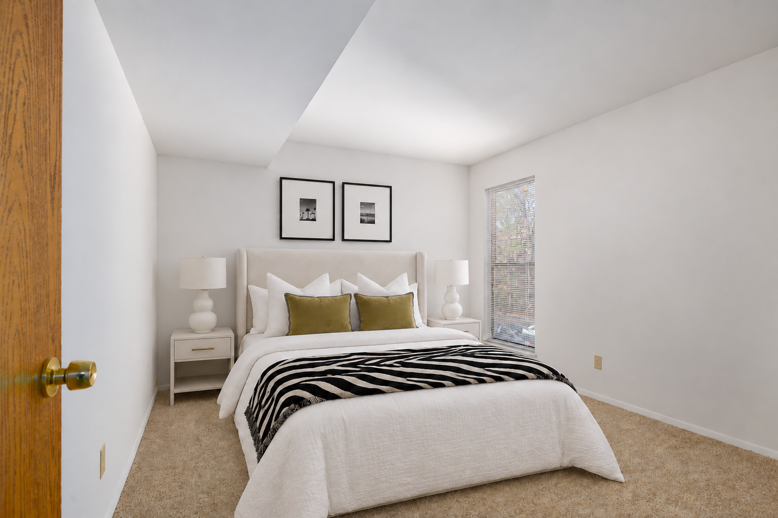 Staged bedroom with neutral bedding and a window at Village Park Apartments
