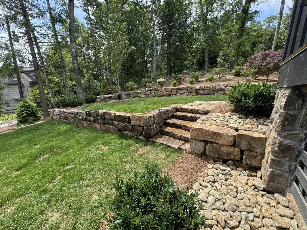 Stone steps and retaining wall in a landscaped garden with trees and green lawn.