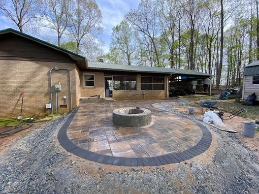 Backyard patio with circular fire pit and curved brick border beside a house and trees