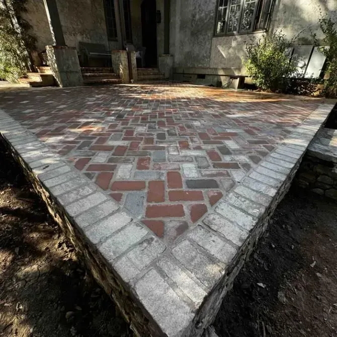 Red and gray brick patio leading to a house entrance, bordered by light stone edging.
