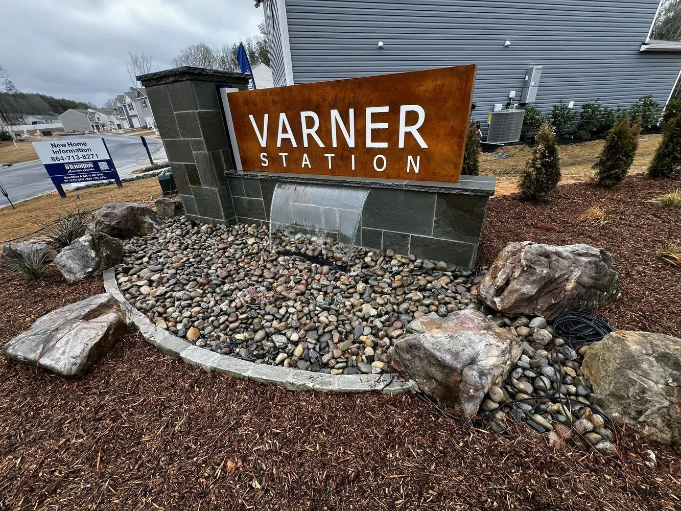 Warner Station sign in a landscaped entrance with rocks, mulch, and shrubs