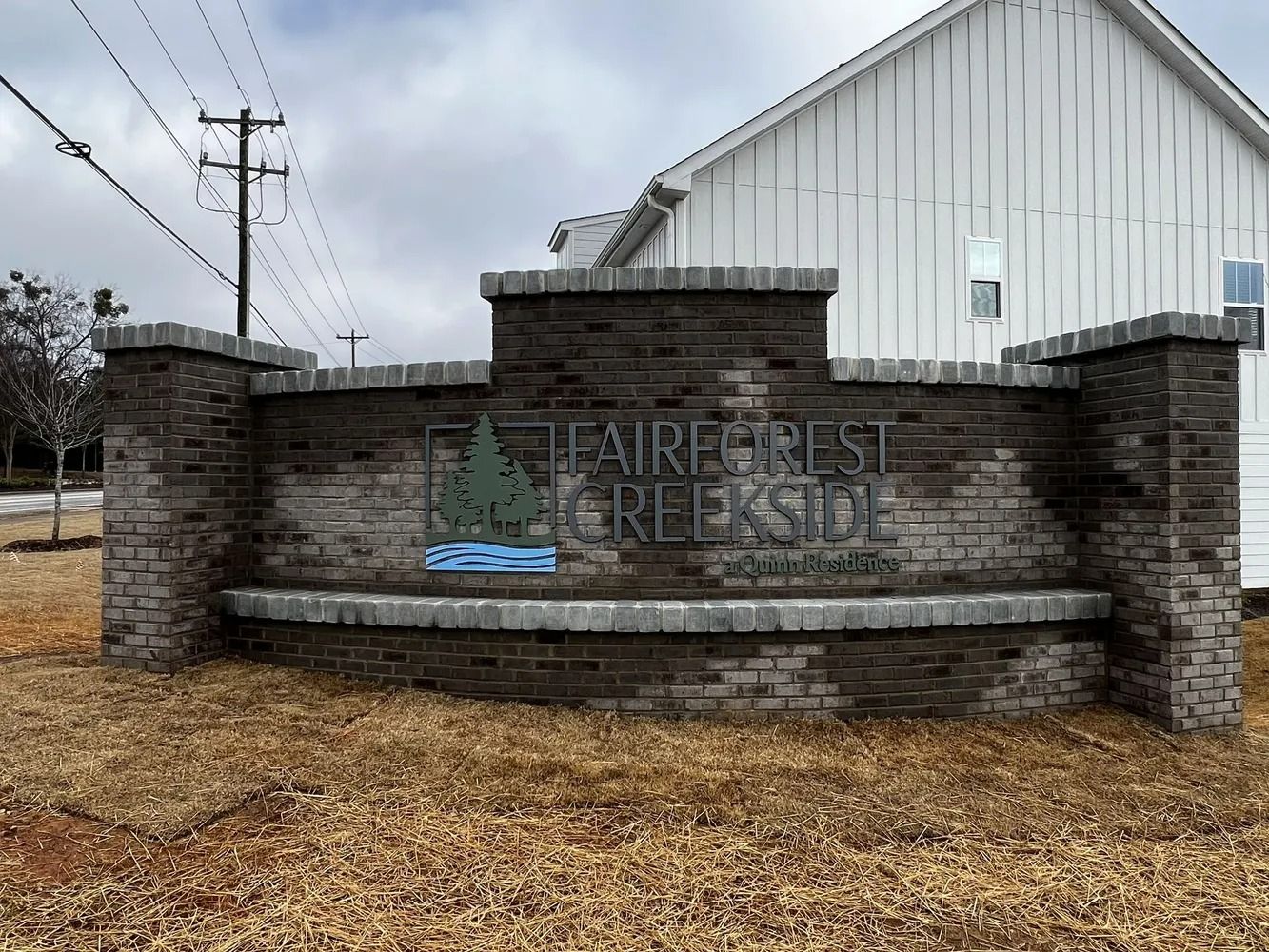 Stone entrance sign for a church or cemetery with faint lettering, in front of a white building and leaf-covered ground