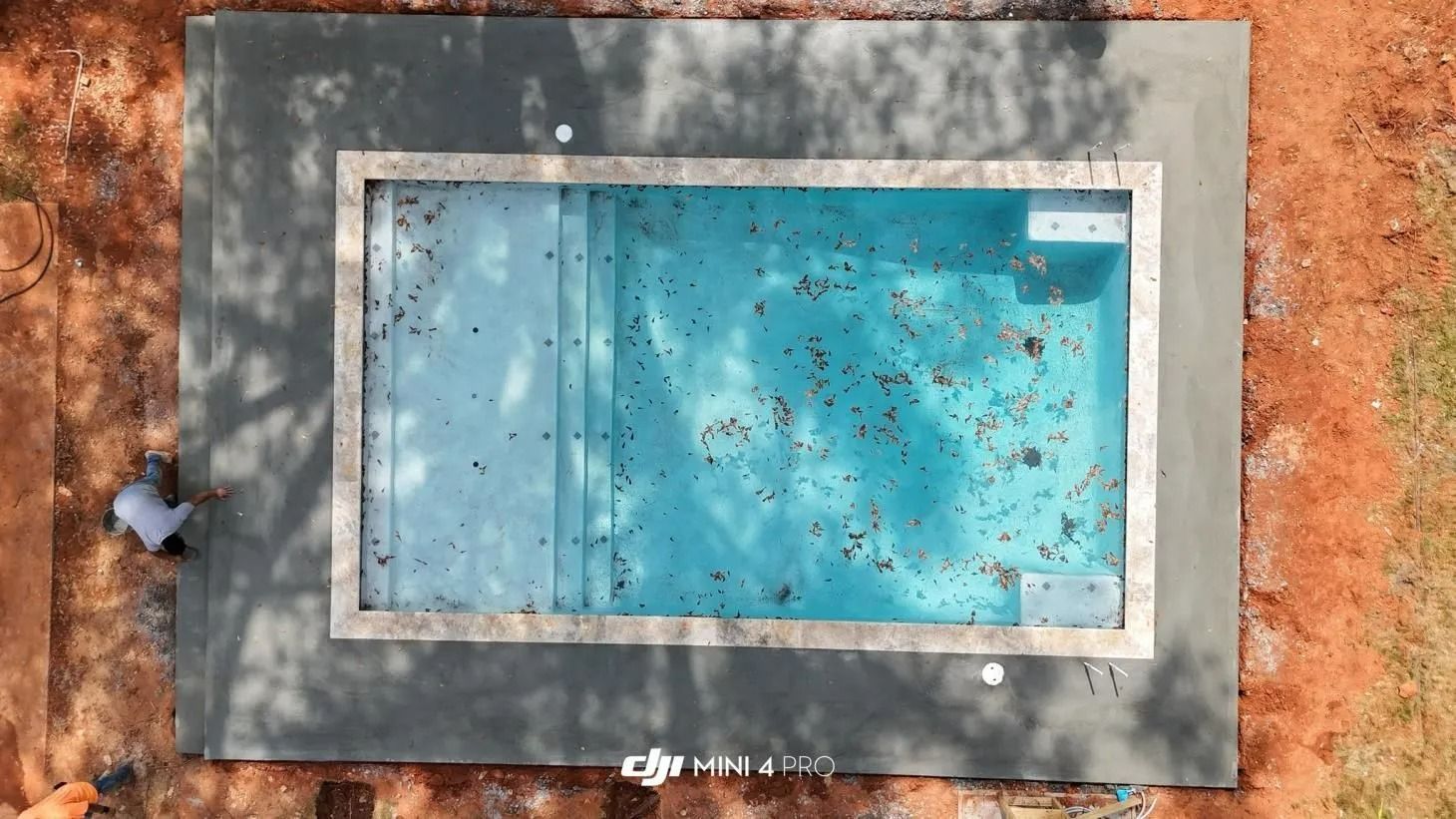 Aerial view of a rectangular blue pool or water tank in a gray concrete enclosure surrounded by red dirt.