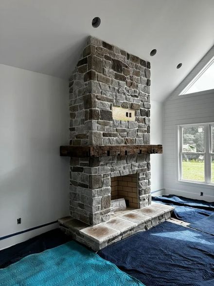 Tall stone fireplace in a bright living room with large windows and blue floor covering