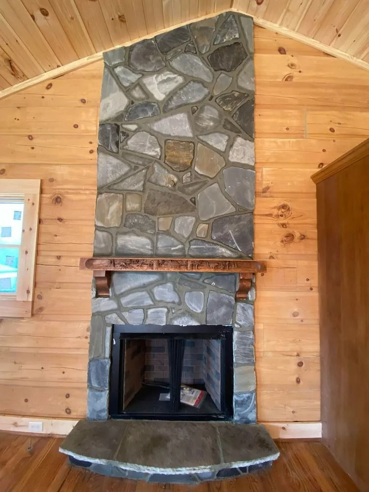 Rustic stone fireplace with wood-paneled walls and a curved stone hearth in a cabin interior