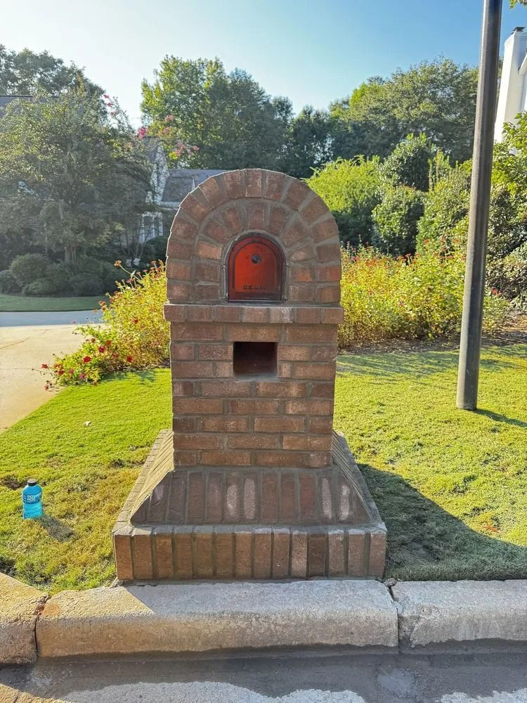 Brick mailbox with arched red front beside a curb and grassy roadside edge