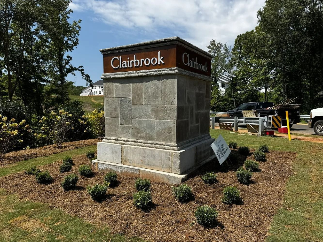 Claybrook stone monument sign with brown top, surrounded by mulch and small shrubs in a landscaped area