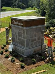 Workers install a stone monument sign reading “Clairbrook” beside a road.
