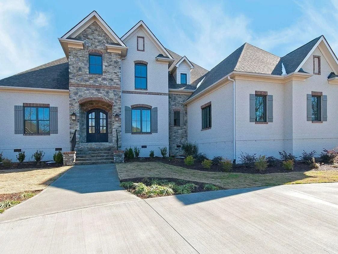 Stone and white stucco suburban house with gabled roof, front walkway, and driveway under a clear sky