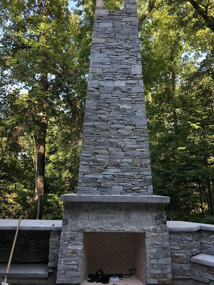 Stone outdoor fireplace with a tall chimney in a wooded setting