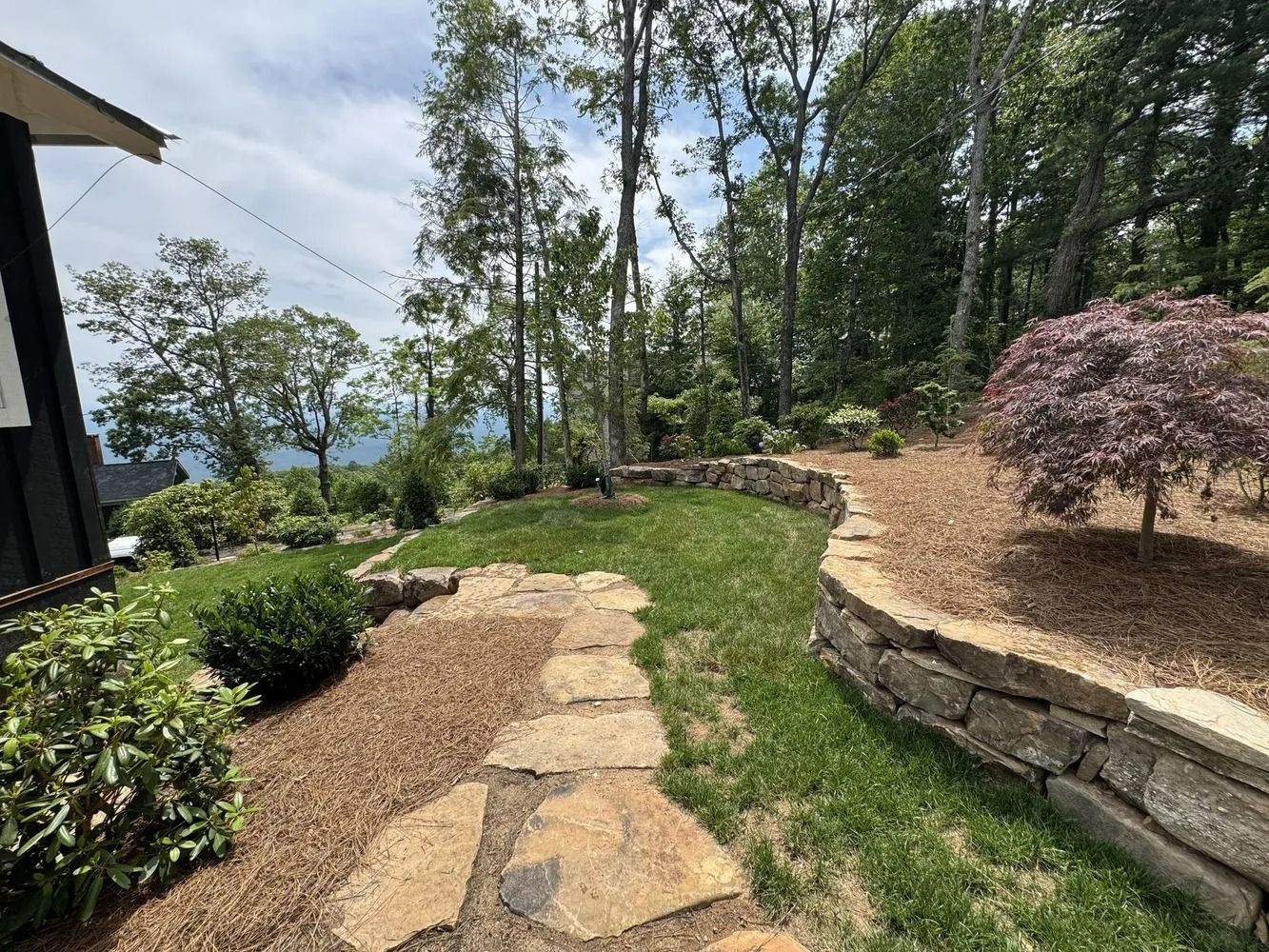Stone path through a landscaped garden with trees, shrubs, and a view toward the water