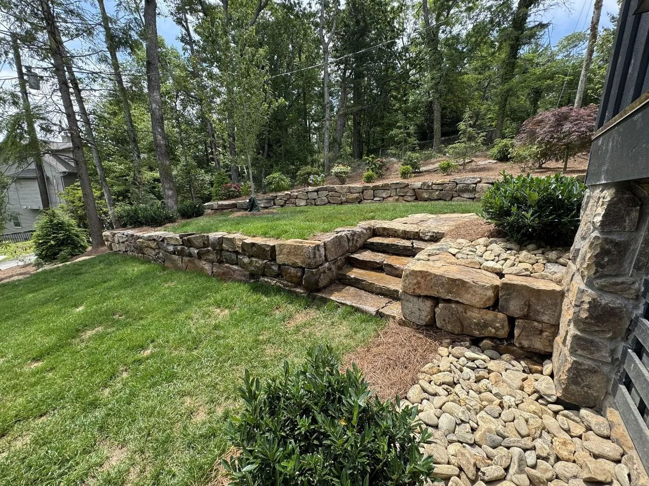 Terraced stone retaining wall and steps in a landscaped yard with trees and green lawn