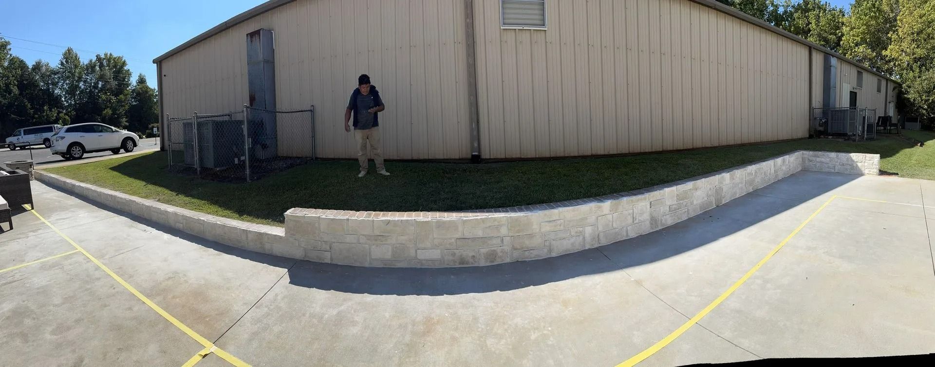 Wide-angle view of a beige building with a person standing by the wall and a curb in front