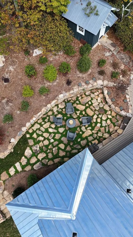 Aerial view of a landscaped yard with stone path, small shrubs, and blue-roofed buildings.