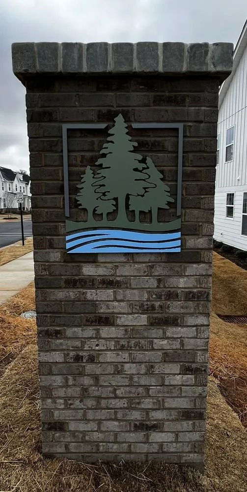 Brick pillar with a green tree emblem and blue waves on a cloudy street corner