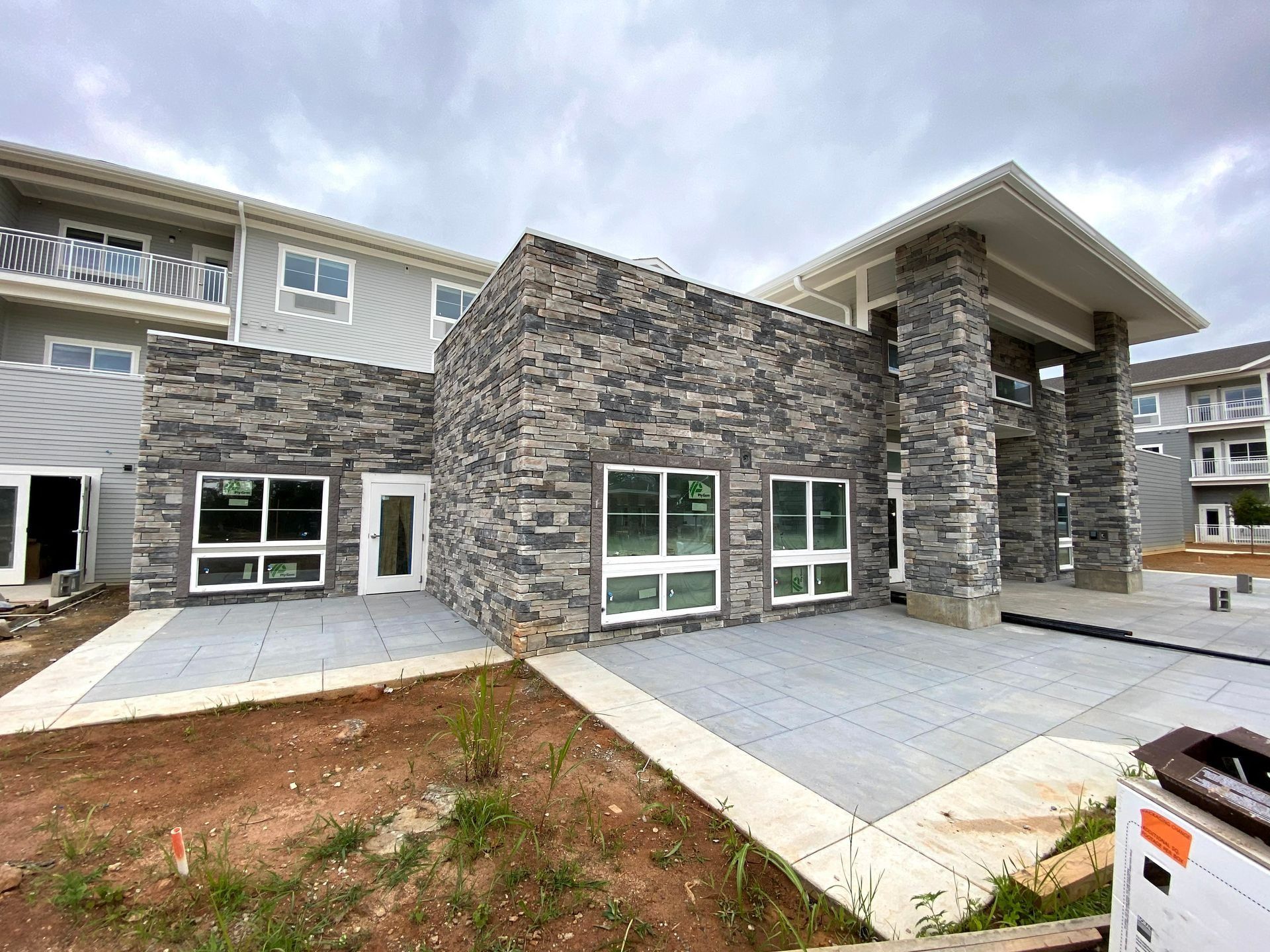 Modern stone apartment building exterior with large windows, patio, and paved driveway